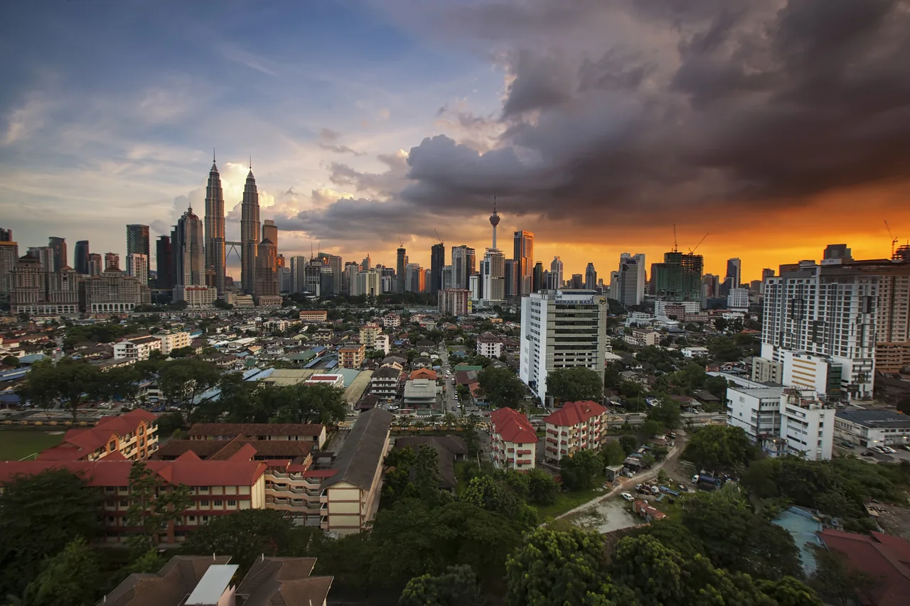 The Kuala Lumpur skyline at dusk, the Petronas Towers among the city towers under a stormy orange sky