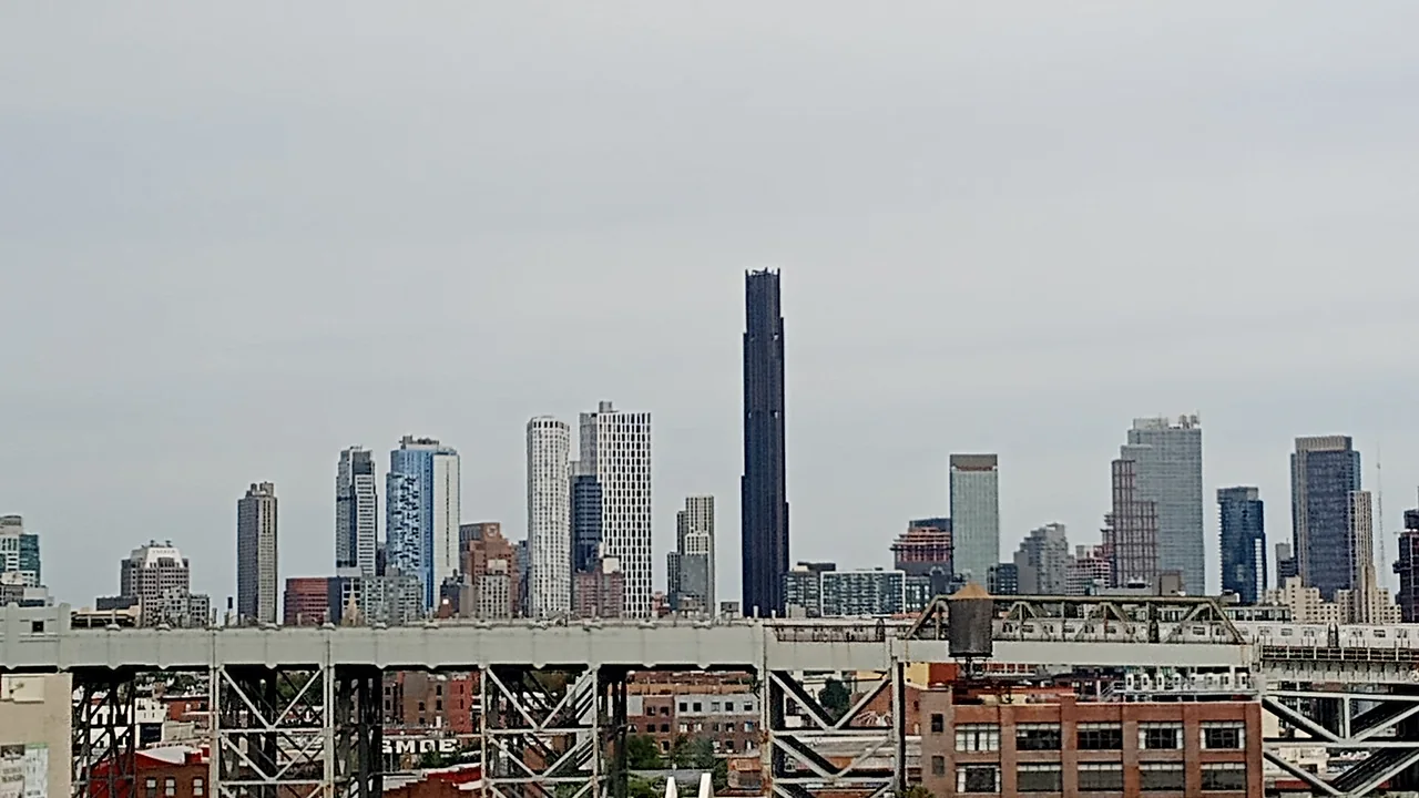 The Downtown Brooklyn skyline against a pale sky, with Manhattan towers beyond